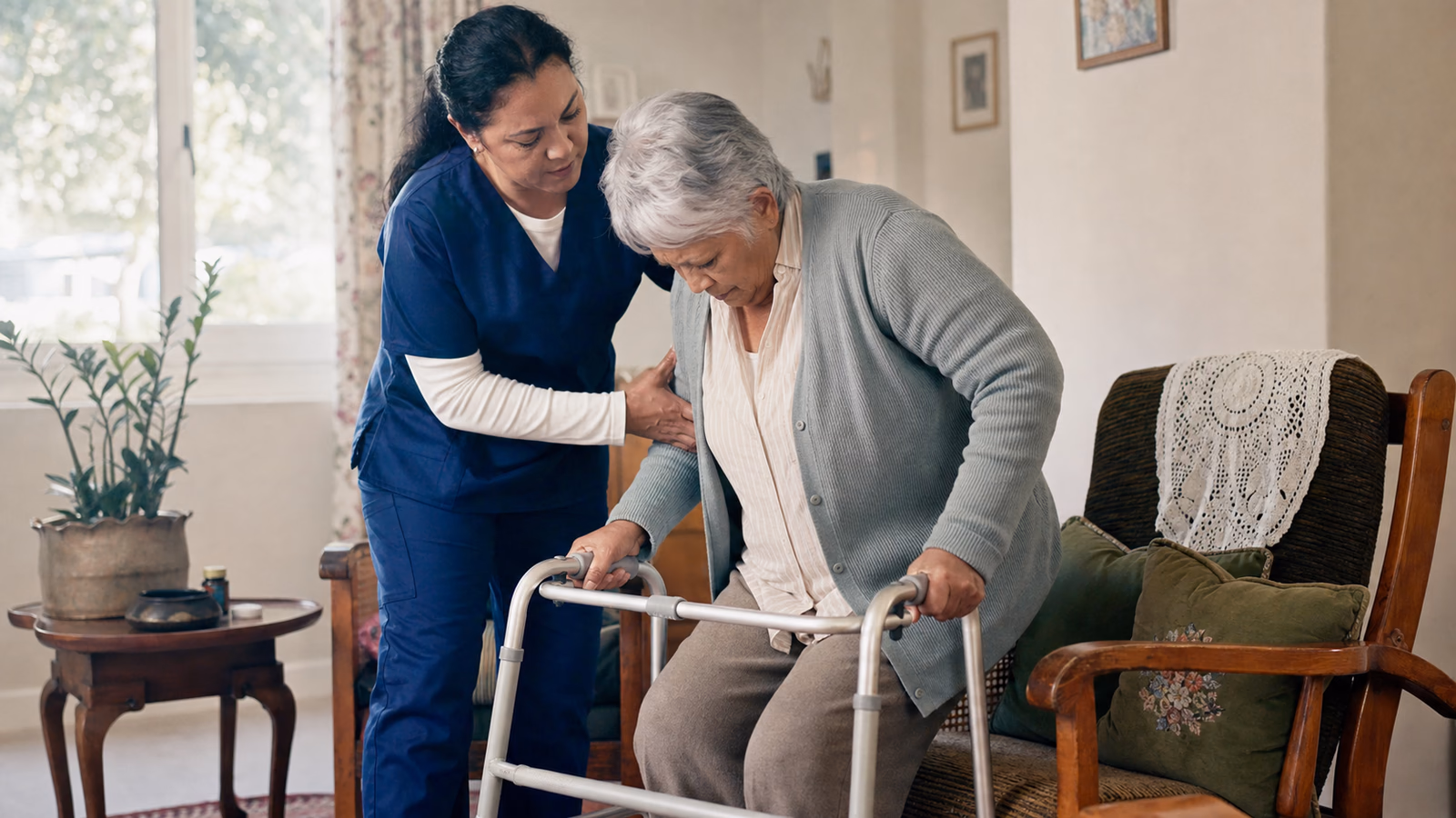 Home-care nurse guiding an older adult safely from an armchair to a walking frame