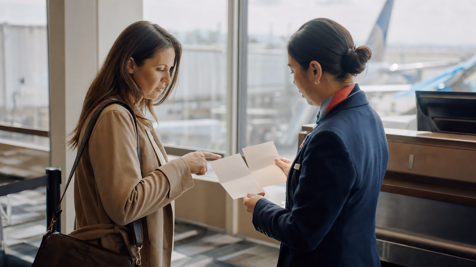Agente de service passagers comparant deux documents de voyage avec un voyageur à une porte d’embarquement