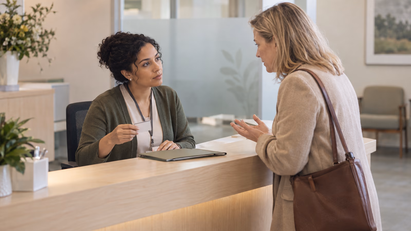 Een baliemedewerker in een kliniek controleert een identiteitsbewijs terwijl zij luistert naar een verzoek om patiëntinformatie
